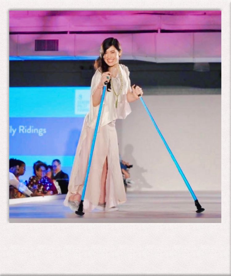 Xian Horn on the CP Foundation Design for Disability runway wearing a custom-made silk top and skirt, holding ski poles, smiling at the camera. 